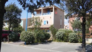 A two-story building with a balcony, surrounded by trees and parked cars. - Beautiful, lovingly furnished holiday home near the beach with sea views (Narbonne)
