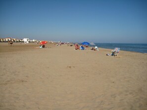 A beach with people sunbathing and walking. There are umbrellas and beach chairs.