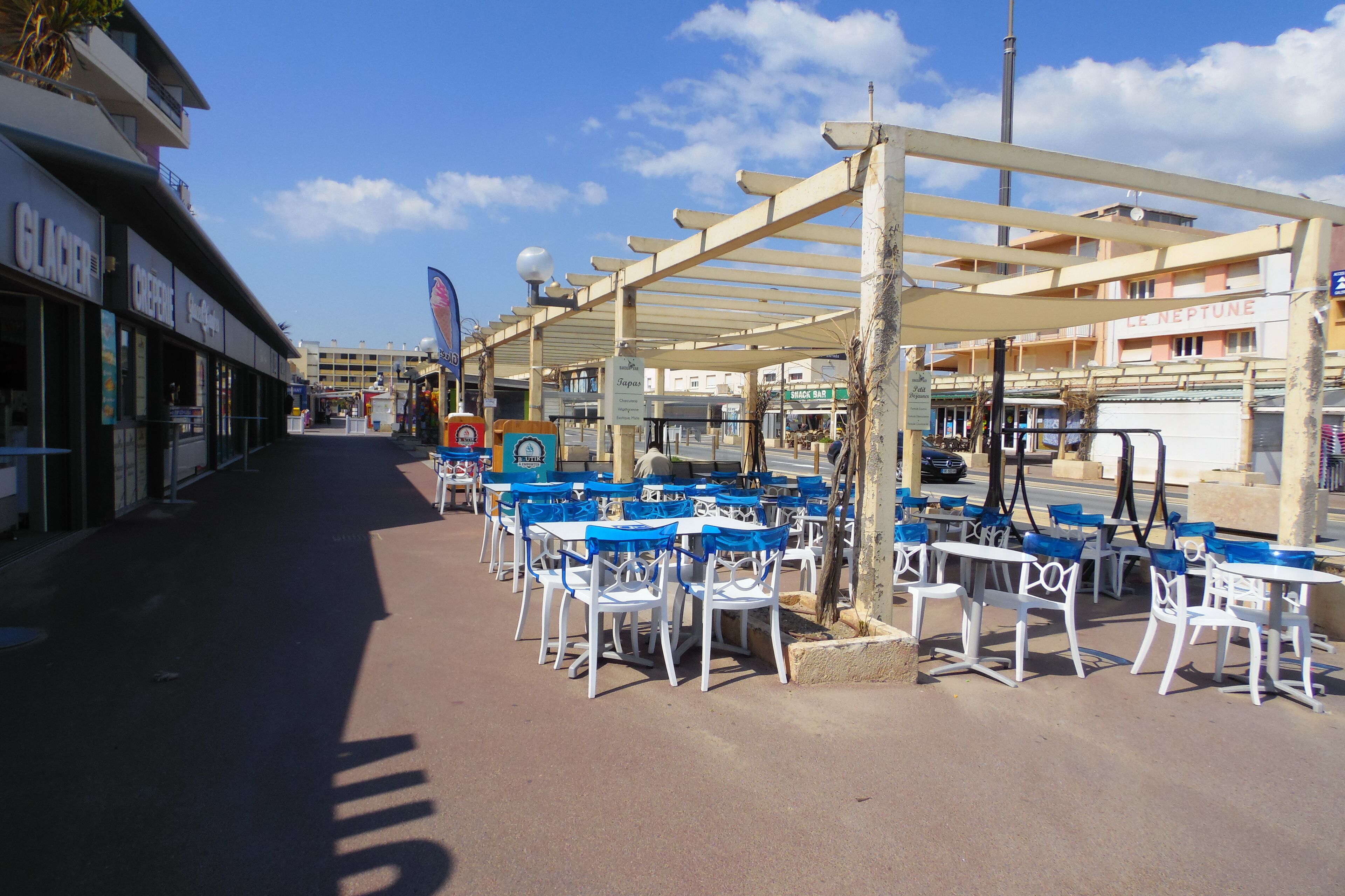 An outdoor seating area with white tables and blue chairs under a pergola, adjacent to a building with a sign that reads "Glacier".