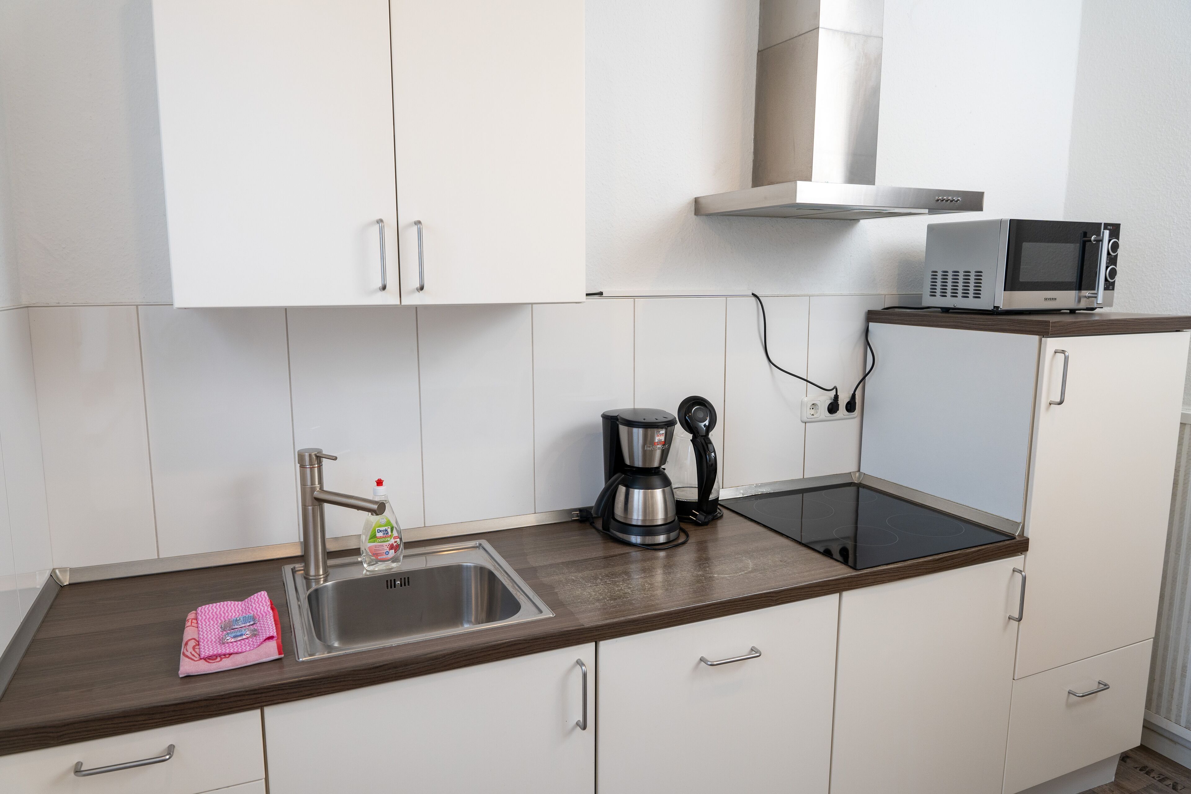 Een moderne keuken met witte kasten, een roestvrijstalen spoelbak, een koffiezetapparaat en een magnetron op een houten aanrecht.