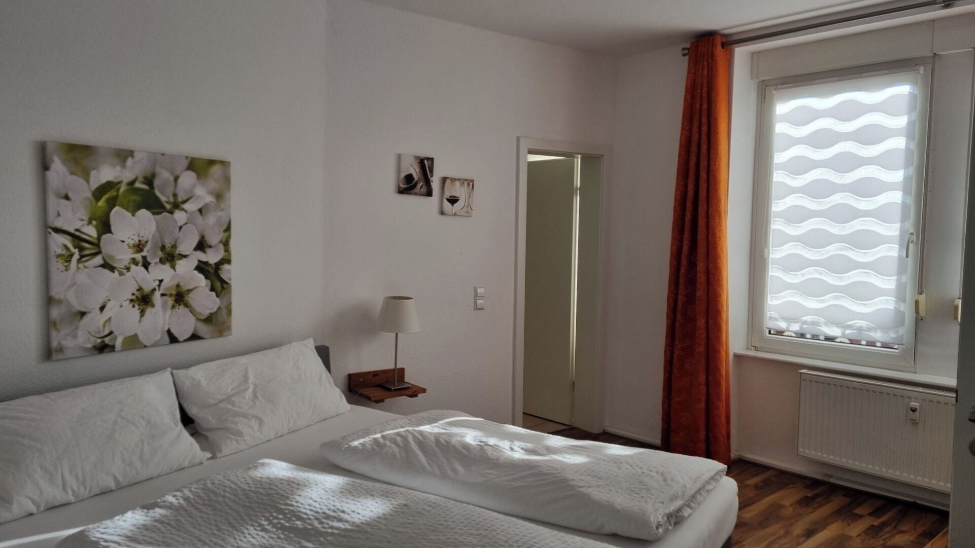 A bedroom with a bed, a nightstand, a lamp, a window with curtains, and a door.