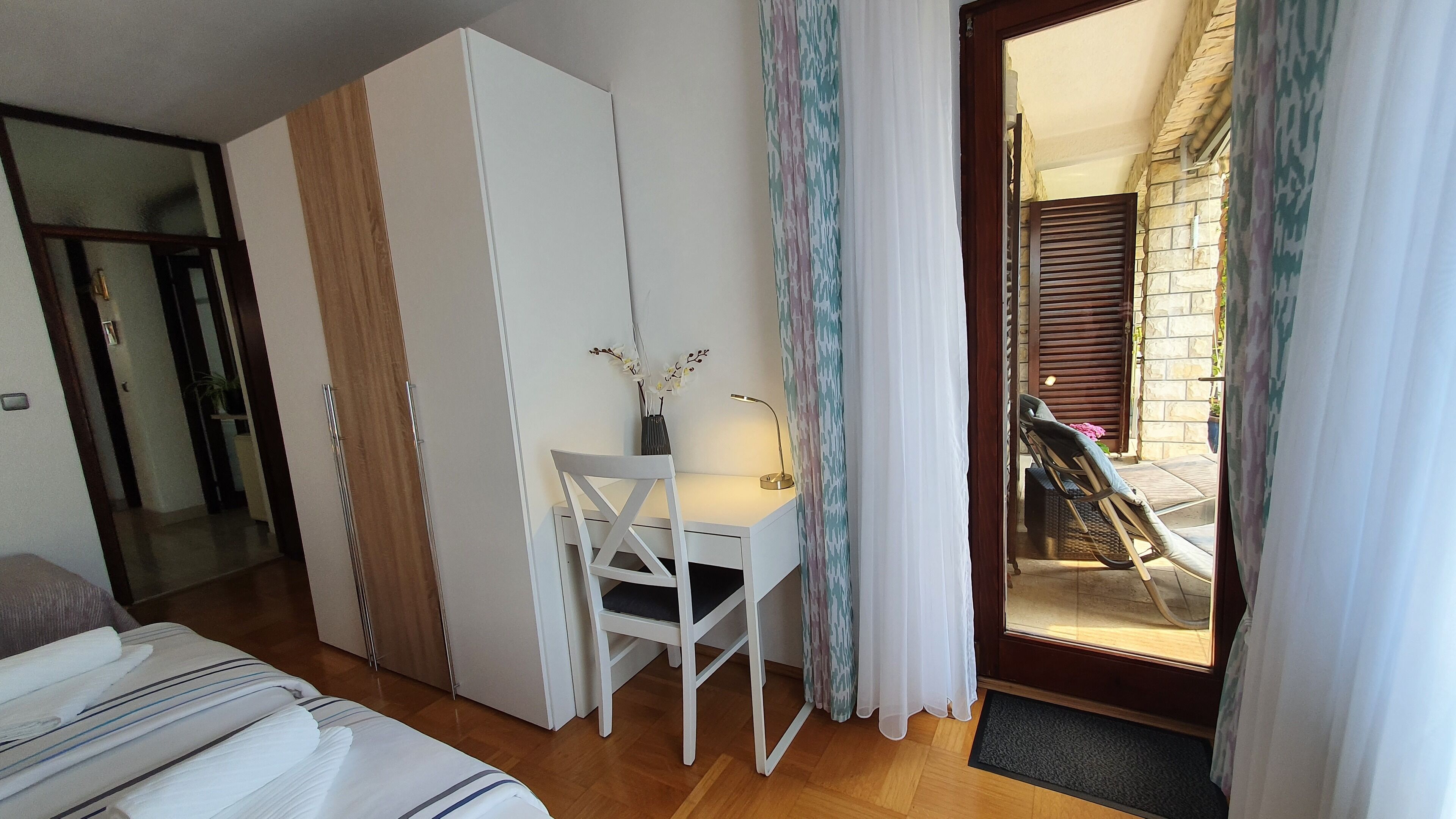 Une chambre à coucher comprenant un lit, un bureau avec une chaise, une armoire et donnant sur un espace extérieur avec un escalier.