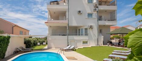 A multi-story building with a swimming pool, outdoor seating, and a well-maintained lawn.