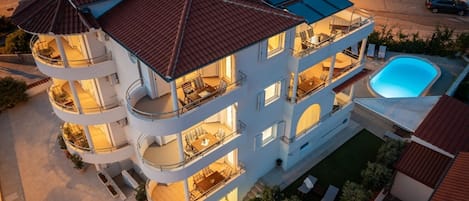 A multi-story building with balconies, a swimming pool, and solar panels.