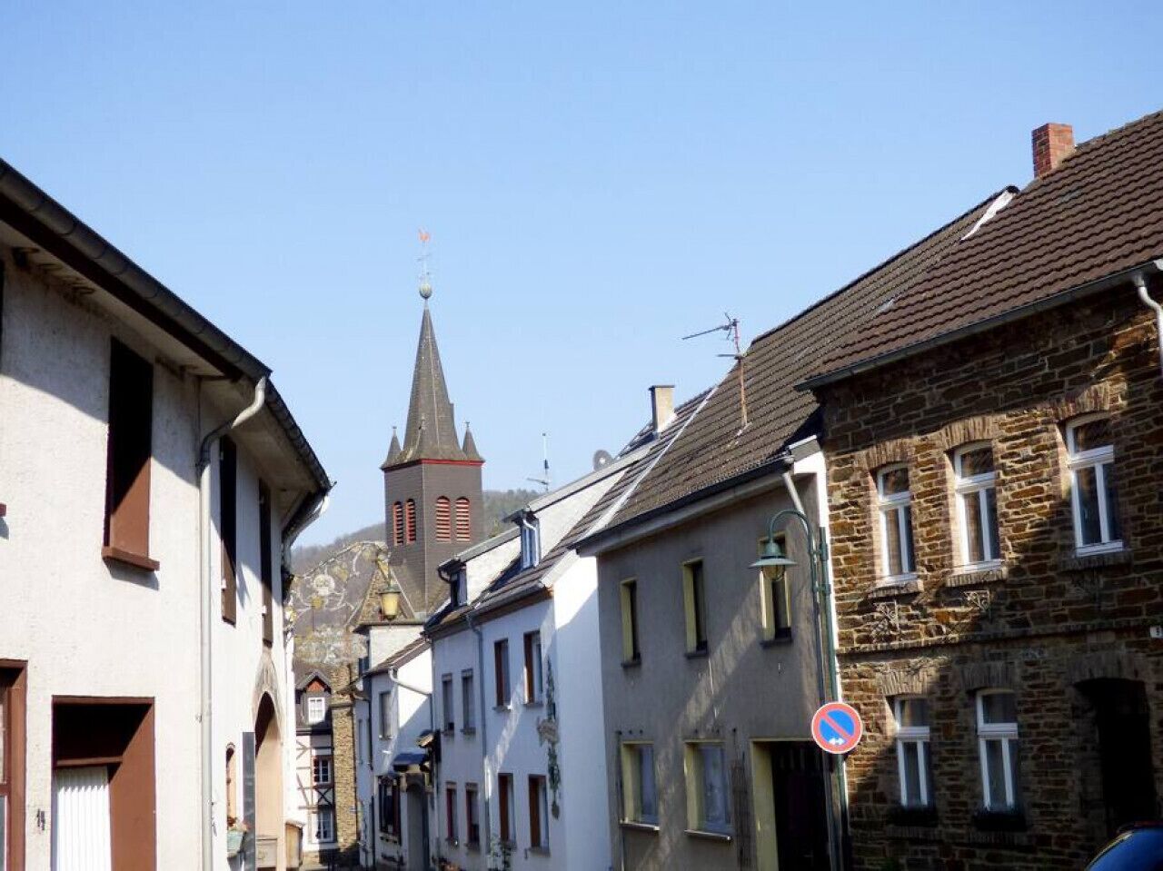 A narrow street with historic buildings, a church spire, and a no parking sign.