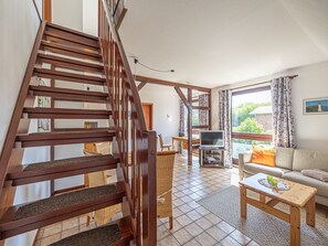 Ein geräumiger Wohnbereich mit einer Holztreppe, einem Fernseher, einer Couch und einem Esstisch.