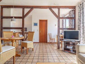 A spacious living area with a tiled floor, wooden furniture, a television, and a large window with curtains.