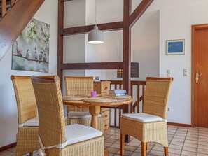 A dining area with wicker chairs, a round table, and a hanging light fixture.