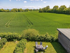 Ein großes grünes Feld mit einem Tisch und Stühlen im Vordergrund, und ein Gebäude zur rechten Seite.