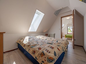 Camera da letto con soffitto spiovente, finestra a lucernario, letto con copripiumino decorato e termosifone.