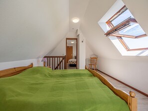 Ein Schlafzimmer mit schrägen Wänden, einem Dachfenster, einem hölzernen Bettgestell und einer grünen Bettdecke.