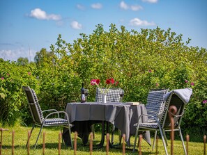 Zona pranzo all'aperto con tavolo e sedie, circondata da vegetazione lussureggiante e cespugli fioriti.