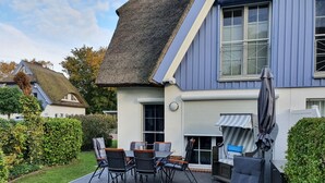Een huis met rieten dak, een terras met tuinmeubilair en een verzorgde tuin.