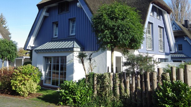 Een traditioneel huis met een steile dakschild, grote ramen en een verzorgde tuin.