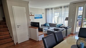 Een moderne woonkamer met een bank, salontafel en televisie. Een trap leidt naar een andere kamer.