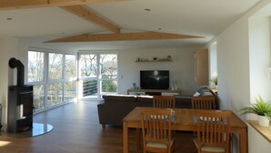 A spacious living area with a large window, a fireplace, a television, and a dining table with chairs. - Fantastic, sunny apartment with Baltic Sea view and balcony near the beach (Langballigholz)