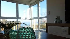 A room with large windows, a wooden table, and decorative glass vases. - Fantastic, sunny apartment with Baltic Sea view and balcony near the beach (Langballigholz)