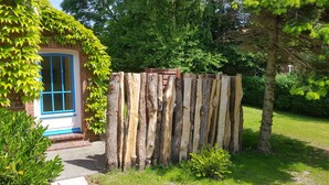 Ein rustikaler Holzzaun in einem Garten mit einem Backsteinhaus und blauen Fensterläden sowie einer Tür.