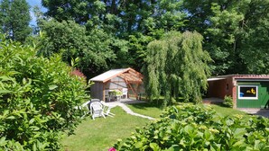 Eine kleine Holzhütte mit einem Metallroof, umgeben von üppiger Bepflanzung und einem Weg dorthin.