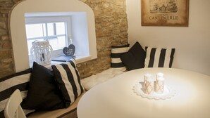 A cozy room with a stone wall, a white round table with candles, black and white striped pillows, and a framed picture of Chateau Cantemerle.