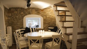 A dining area with a stone wall, a round table, and white chairs.
