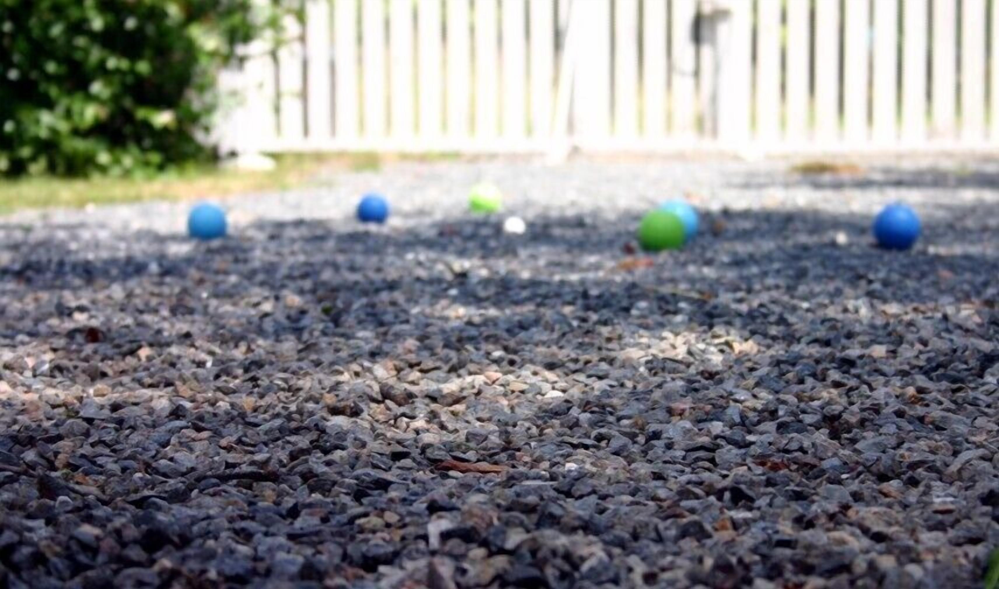 A gravel surface with several blue and green balls scattered across it.
