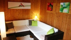 A wooden-paneled room with a white sofa, green cushions, and wall art depicting a bird, strawberries, and apples.