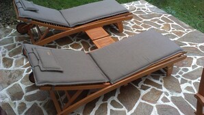 Two wooden lounge chairs with cushions on a stone-tiled patio.
