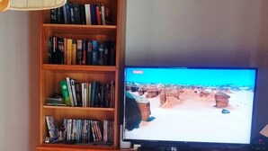 A living room with a wooden cabinet, a television, a round wooden table, and a remote control.