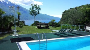 Una piscina con vistas a un lago y montañas. Hay sillones de descanso y una mesa de picnic.