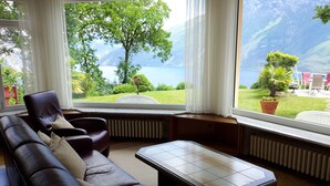 Una sala de estar con sofá de cuero, una mesa de centro y vista a un lago y montañas a través de amplios ventanales.