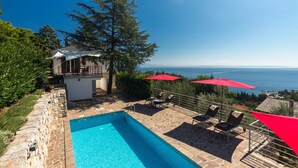 A pool area with stone flooring, red umbrellas, and a view of the sea. - Villa Capra Verde - private pool, oasis of peace, 150 m as the crow flies to the sea, Opatija  (Icici)