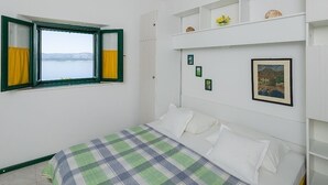 Ein Schlafzimmer mit Bett, einem Fenster mit Vorhängen, einem Regal mit Dekoration und gerahmten Bildern an der Wand.