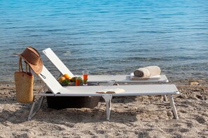 Een strandligbed met een strooien tas, een opgerolde handdoek en een glas sinaasappelsap.