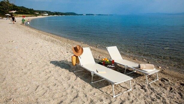Une plage avec deux chaises longues, un chapeau de paille et une boisson posée sur le sable.