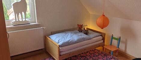 A bedroom with a bed, a window with a deer silhouette, a radiator, a wooden chair, and a red lantern.