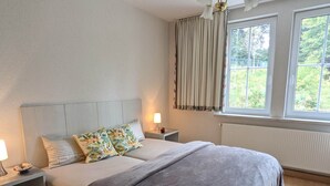 A bedroom with a bed, nightstands, a lamp, a window with curtains, and a ceiling light fixture. - Historic villa & comfort in the biosphere reserve (Vesser)