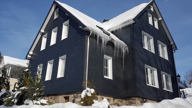 A two-story house with a steeply pitched roof, white window frames, and icicles hanging from the eaves. - Historic villa & comfort in the biosphere reserve (Vesser)