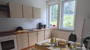 A kitchen with a dining table set for two, a stove, cabinets, and a window with a view. - Historic villa & comfort in the biosphere reserve (Vesser)