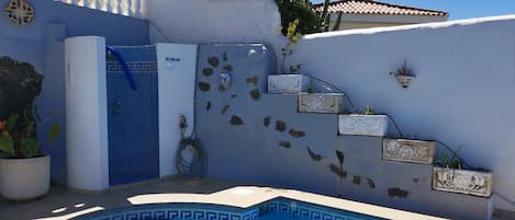 Ein Swimmingpool mit blauen Fliesen und Stufen, umgeben von weißen Wänden mit Zierfliesen und Pflanzen.