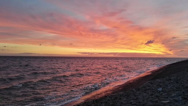 Una playa con costa rocosa y un atardecer sobre el océano.