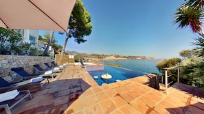 A poolside area with lounge chairs, a small pool, and a view of the sea.