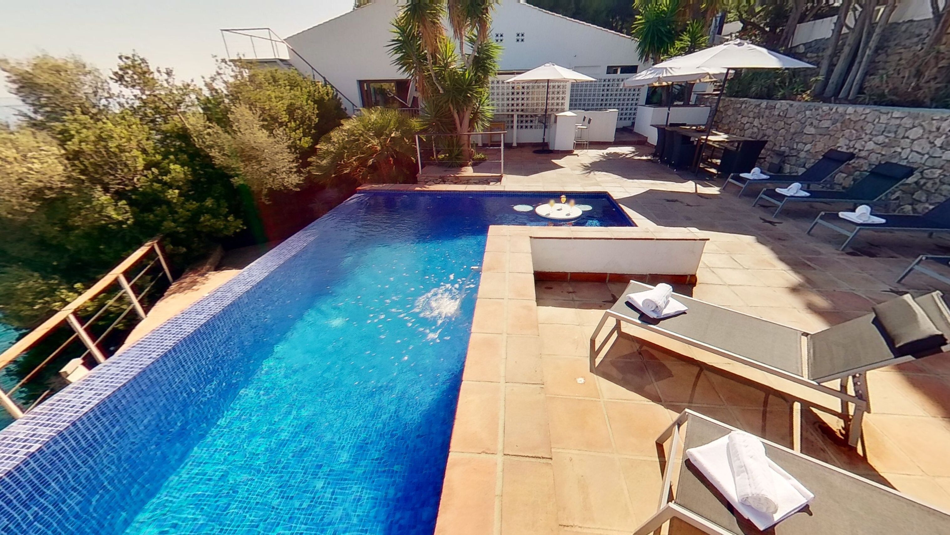 A swimming pool with a tiled edge, a sun lounger, and a small hot tub area.