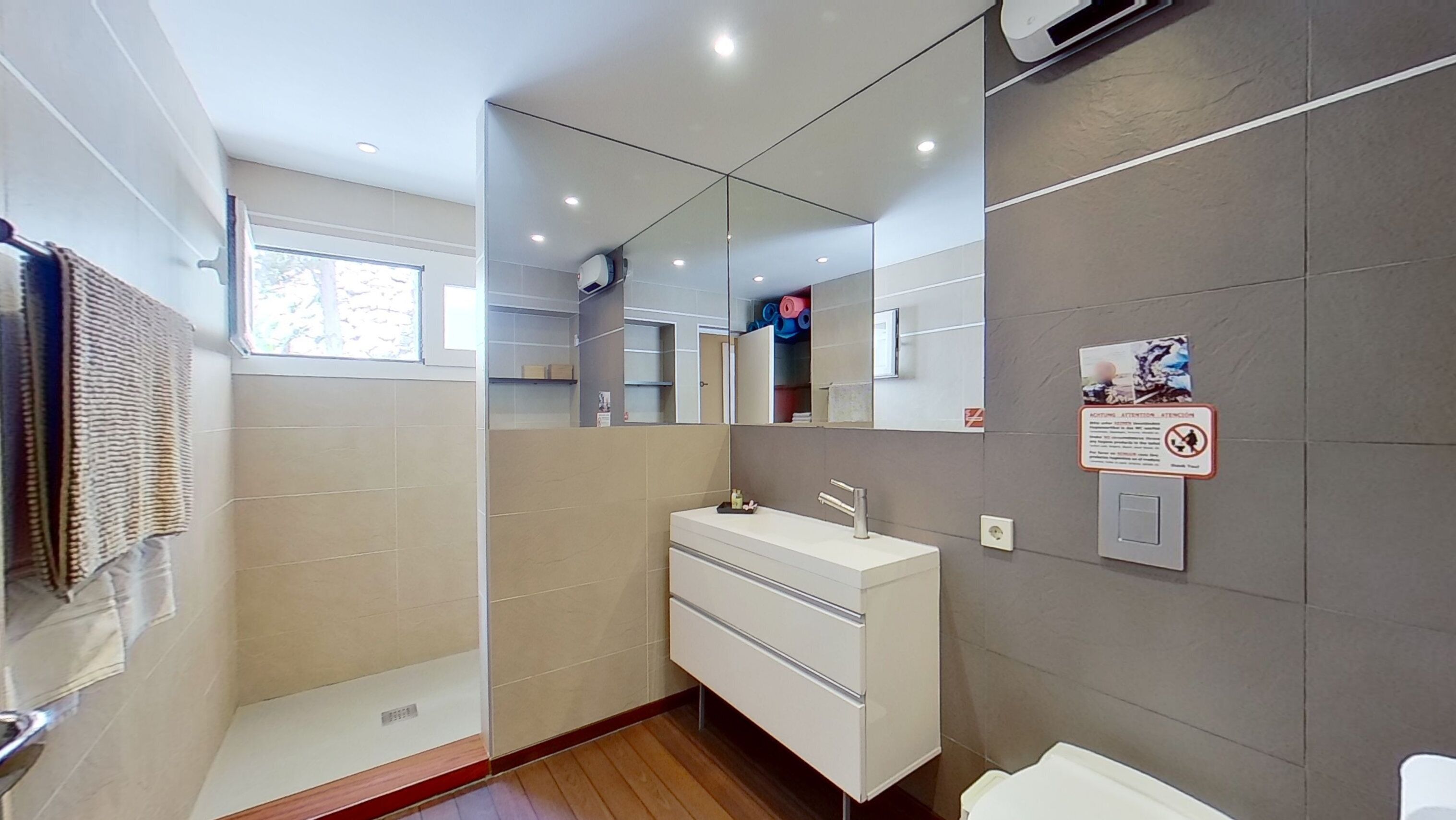 A modern bathroom with a large mirror, a shower, and a toilet.