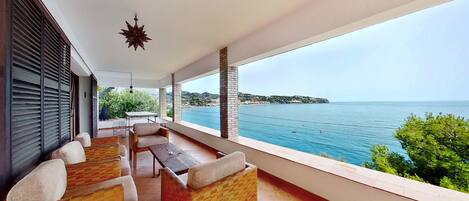 A balcony with a view of the sea, furnished with a table and chairs, and a hanging star-shaped decoration.