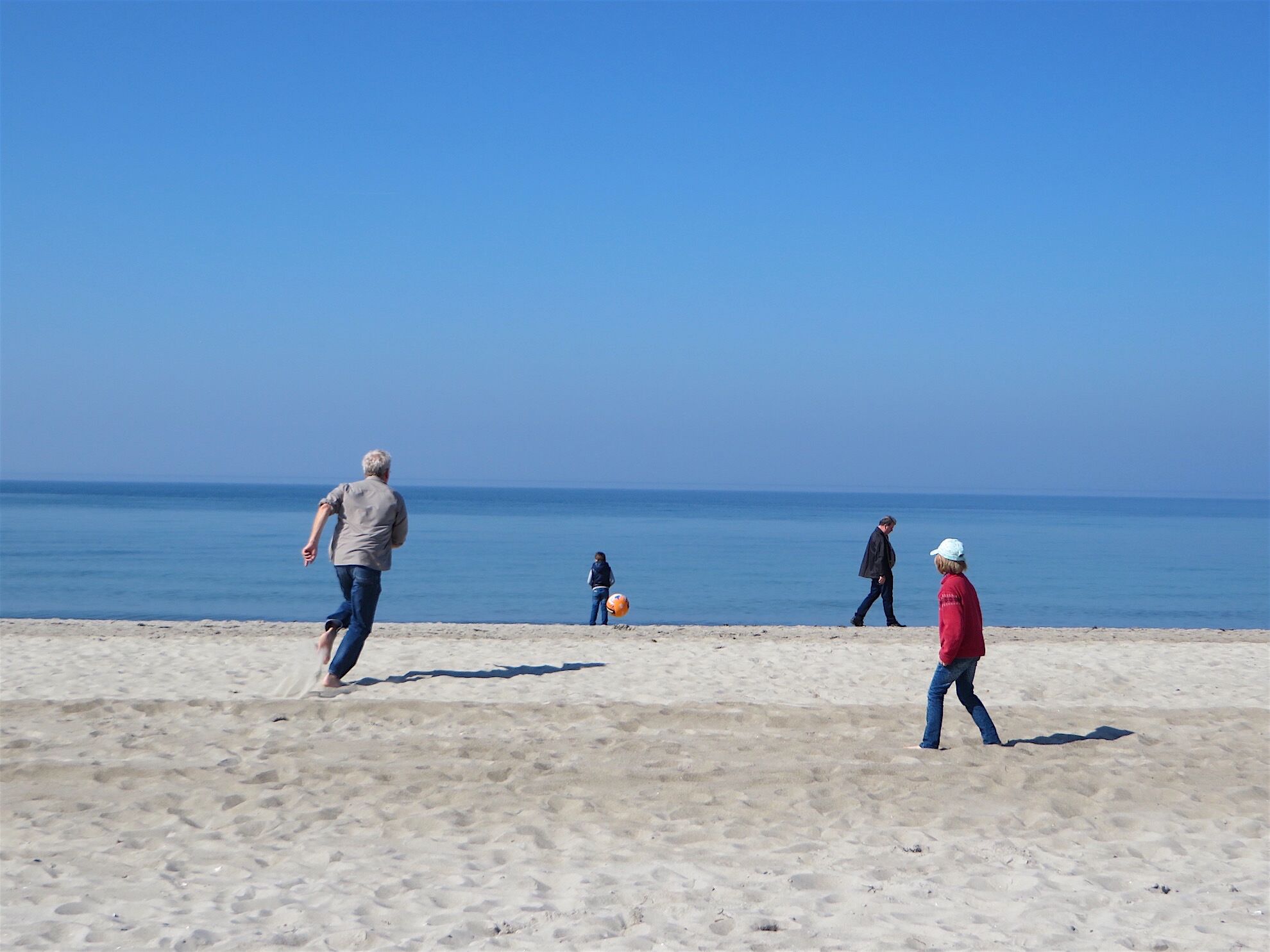 Ein sandiger Strand mit Menschen, die spazieren gehen und spielen.