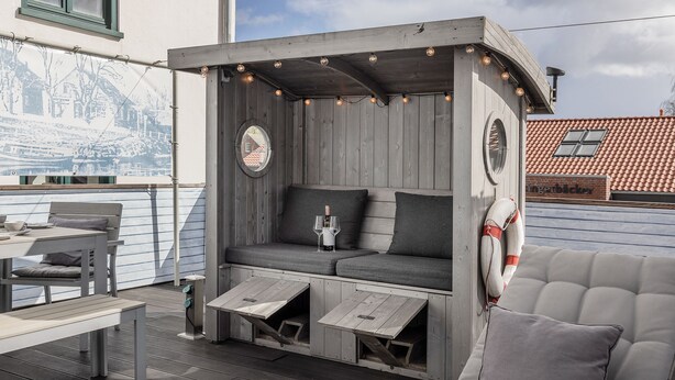 Un espacio exterior acogedor con un banco de madera, un banco acolchado con un vaso y un flotador.