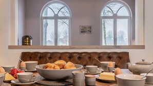Un desayuno con una mesa dispuesta para dos, que incluye un bol de pasteles, huevos y mantequilla.