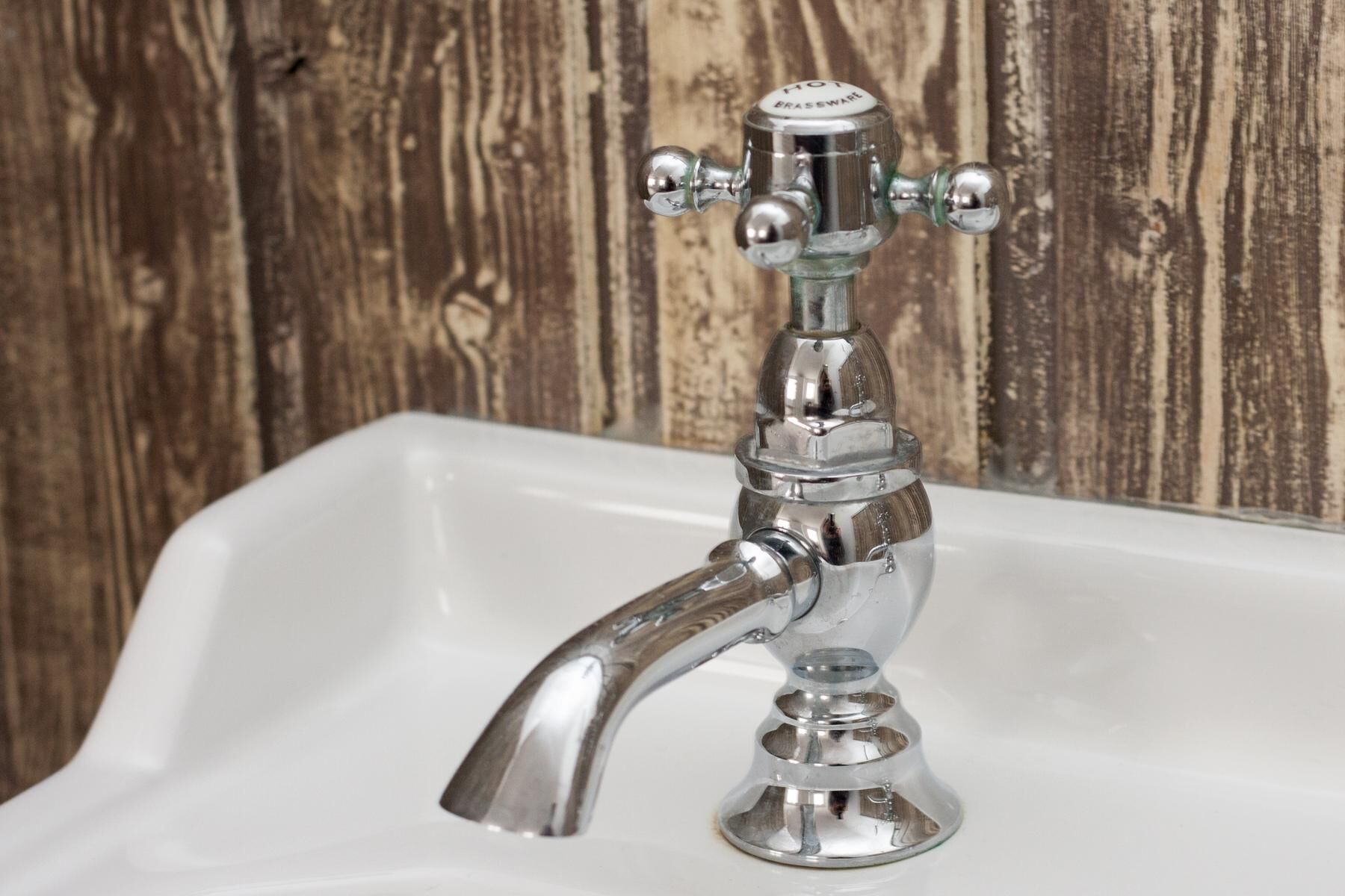 A chrome bathroom faucet with a single handle and a spout, mounted on a white sink against a wooden wall.