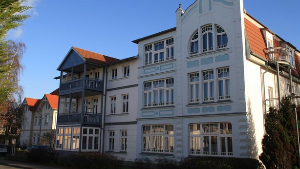Ein mehrgeschossiges Gebäude mit Balkonen, großen Fenstern und einem roten Ziegeldach.
